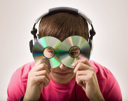 Portrait of an unidentified cheerful young guy in headphones putting two CDs on his face on a white background. Concept of music lover and hobbyの写真素材