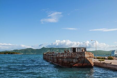 View of old rusty argosy near pier in Ionian sea. Beautiful landscape of Corfu island, mountains on...