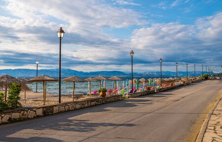 Amazing road near bay with clear water on Corfu island, Greece. Beautiful landscape of Ionian sea beach with colorful chaise lounges and staw umbrellas.の写真素材
