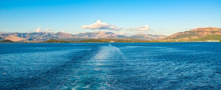 Amazing sealine with crystal clear water, trail after boat, Greece. Beautiful landscape of Ionian sea, island on background. Sunny weather.の写真素材
