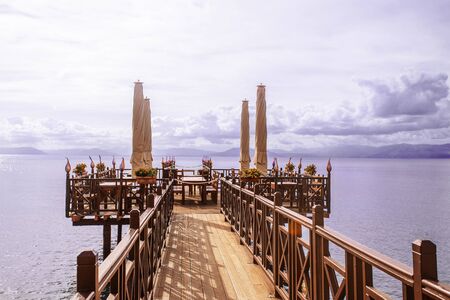 Long wooden pier with romantic cafe in end in Ionian sea. Greece. Beautiful lanscape, mountains on sealine. Sunny day with clouds on Corfu island.の写真素材