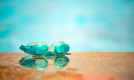 Close-up of waterproof children's swimming goggles lie on a wooden surface against the background of a blurred pool on a warm summer day. Concept of vacation with children at sea. Advertising spaceの写真素材