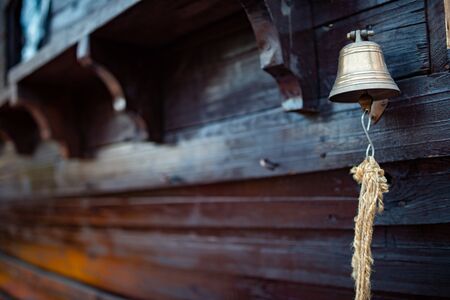 Bell with a rope hangs on the hull of a wooden ship. Concept of notifications and and emergency situations on the ship. Advertising spaceの写真素材