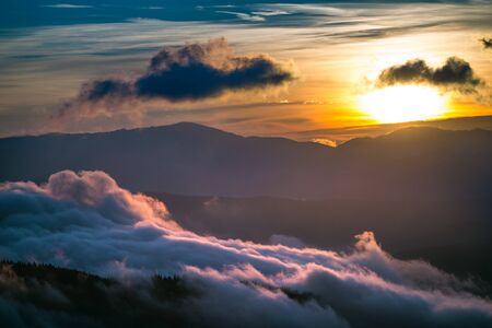 View of beautiful sunset in mountain valley. Hills surrounded by clouds with dramatic sky on background. Concept of nature beauty and sundown.の写真素材