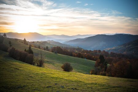 View of magnificent landscape with bright colorful sky over morning valley and mountains. Amazing sunrise in farm field with haystack on grassland over rolling hills. Concept of nature.の写真素材