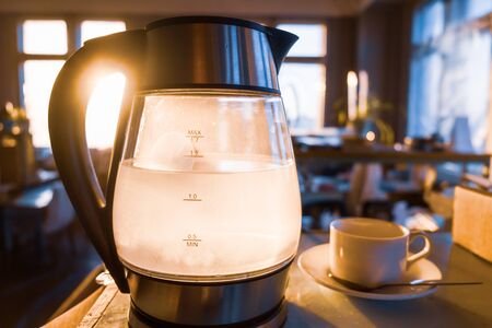 A transparent kettle of water boils against the background of the sunset shining through the window....