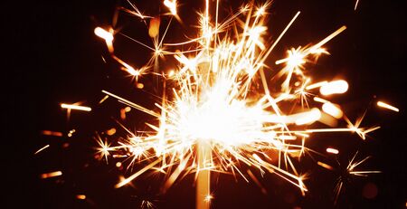 Close-up of golden blurry sparks burn in the dark from the light of festive candles. The concept of fireworks and congratulations on the holidays and happy new year. Copyspaceの写真素材