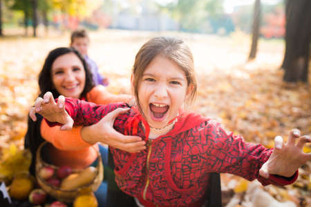 Lovely positive young mother with her screaming daughter walks in the park among the autumn leaves....