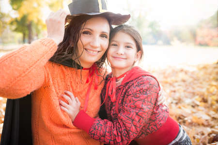 Lovely positive young mother In a paper hat with her smiling little daughter walks in the park among...
