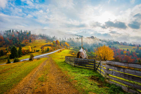 View of scenic landscape with bright colorful sky over foggy mountains. Majestic sunrise in misty morning valley with haystack on grassland hill. Concept of nature.の写真素材