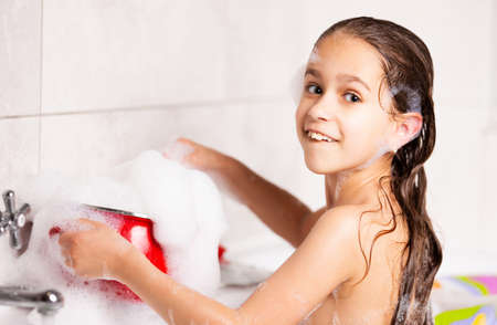 Cheerful little caucasian girl plays with foam while bathing in the bathtub during quarantine. Concept of funny kids have fun at home during coronavirus. Copyspaceの写真素材