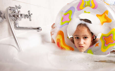 Funny little girl bathes in a bathtub with an inflatable lifebuoy and with foam in the water....