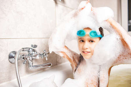 Beautiful blue-eyed little girl in swimming goggles bathes in a foam bath while enjoying a summer...