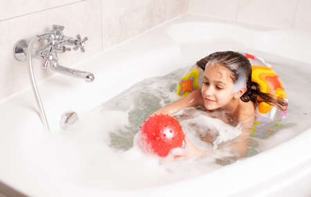 Little girl have fun in the bathtub and plays in the inflatable red ball while sitting in the...