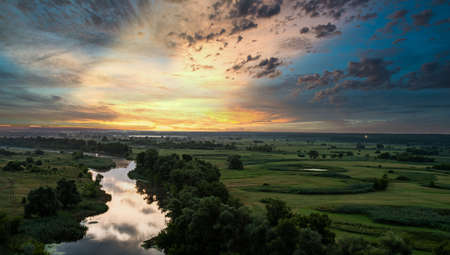 Panoramic view from hill of fantastic landscape of dramatic colorful sky, amazing sunset. Beautiful scenic lanscape of river with clear silent water between green fields and forests in summer evening.の写真素材