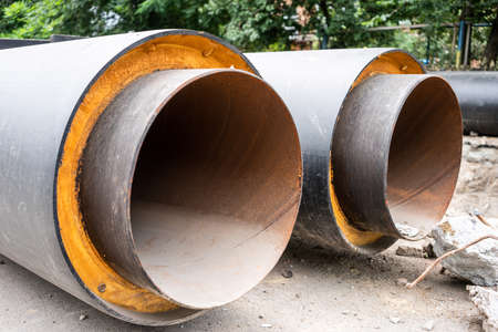 Closeup view of two new insulated water pipes on city road in summer day. Urban sewerage...