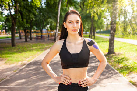 Fit woman with kinesiological taping posing outdoors.