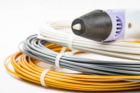 Closeup view of bunch of colorful rolled cables and childrens 3D printing pen isolated on white. Three bright filament plastic lying indoors. Concept children's entertainment and creativity.の写真素材