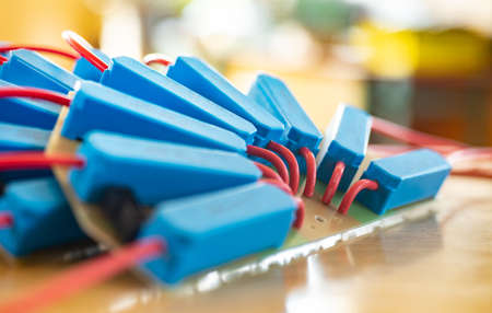 Close-up of a large green microcircuit with red HI-voltage wires and blue relays connected to it at...