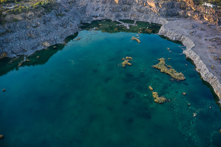 Old flooded stone quarry with large stones in the evening warm bright light covered with small dry...
