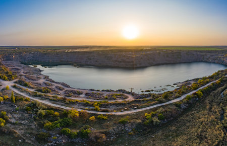 Old flooded stone quarry with large stones in the evening warm bright light covered with small dry plants in picturesque Ukraine. Aerial panoramic drone shotの写真素材