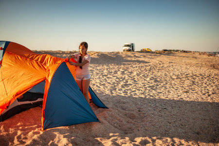 Beautiful young girl with dark hair sets up a tent on the beachの写真素材