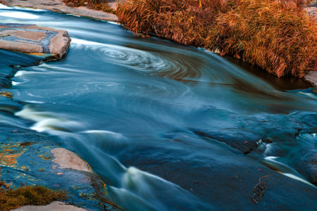 Stream runs among white wet stones covered with grass in golden autumnの写真素材
