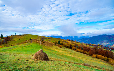 View of scenic landscape with bright colorful sky over foggy mountains. Majestic sunrise in misty morning valley with haystack on grassland hill. Concept of nature.の写真素材
