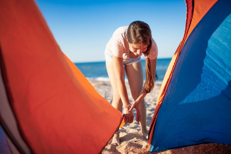 Young girl closes the tent looking at her actions on the blue sea shoreの写真素材