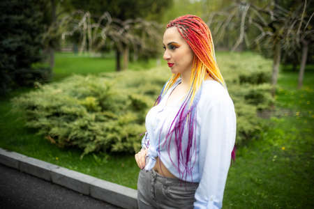 Confident girl with colored makeup and colored braids in fashionable clothes posing against the...