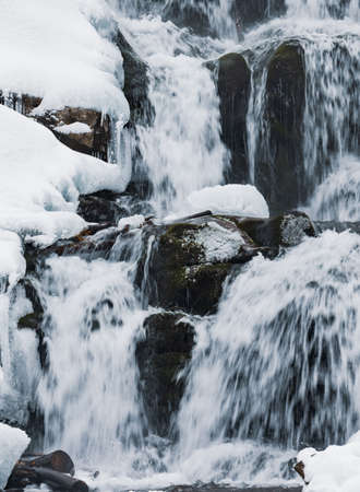 Small waterfall of cold water flow among the stones covered with snowの写真素材