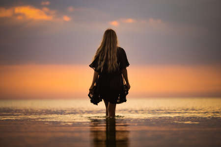 A girl with blond chic hair in a black bikini and a lace shawl walks along the estuaryの写真素材