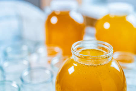 Composition of a large number of transparent empty glass jars and three large glass transparent jars with yellow sweet honey, standing on a large white table against a background of bright sunlightの写真素材