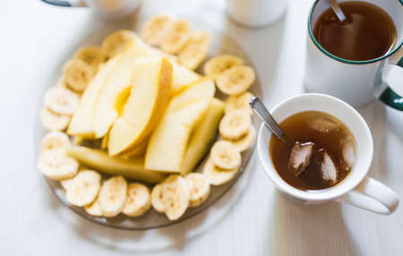 Breakfast with tea and coffee, pieces of fruit, toast with butter and nuts on the table in the kitchen in the morningの写真素材