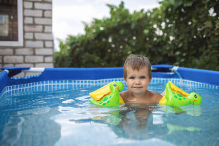 Kid in oversleeves swims in the pool in the yardの写真素材