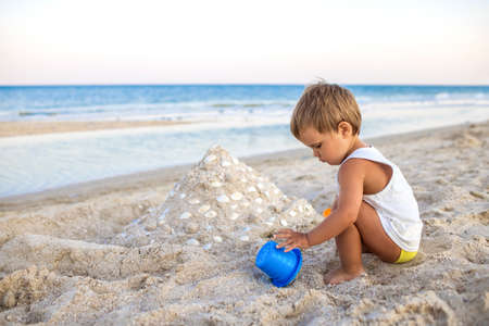 Boy playing with toys on the beach building beads and turrets smiling at someone behind the scenes on summer vacationの写真素材