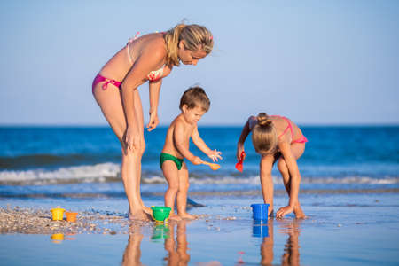 Mom plays with her children: daughter and baby, building beads and castles decorating them with shellsの写真素材