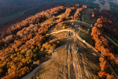 Cableway leading to mountain ridge and ski pistes stretching along hill slopes under white clouds floating on blue sky on autumn dayの素材 [FY310179707324]