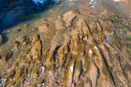 Long rocky river stream with rapids at foothill of high mountain with coniferous terracotta forest...