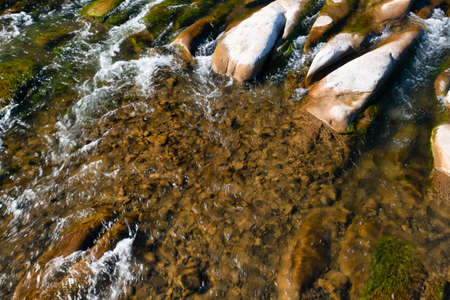 Long rocky river stream with rapids at foothill of high mountain with coniferous terracotta forest...