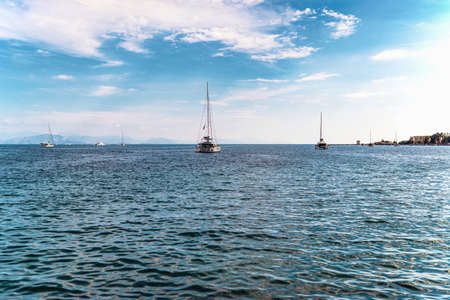 Yachts with deflated sails drift on calm sea water under blue sky with white fluffy clouds near...