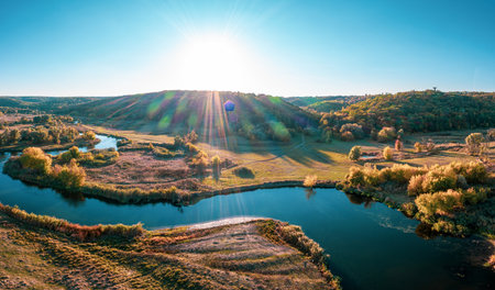 Country ground road stretching between green meadows and long narrow rivers with dark water under blue cloudless sky panorama viewの写真素材