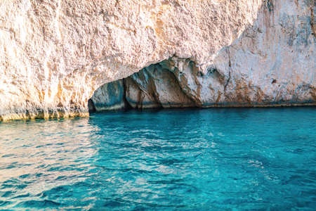 Layered light-colored rocks creating dark cave in sea beach of Corfu island in Greece with clear turquoise water reflecting stonesの写真素材