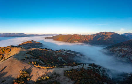 Thick fog among peaks of high autumn mountains at sunriseの写真素材