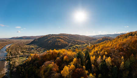 High mountain peak with green and red-colored forests and colorful yellowed meadow under cloudy sky at bright sunset panorama viewの写真素材