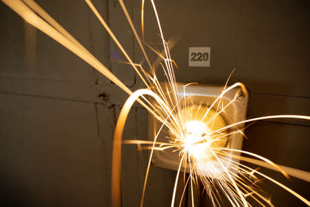 An old faulty outlet with a broken 220 volt power cord plugged in, sparkles with bright electrical dangerous sparks and produces a short circuitの写真素材