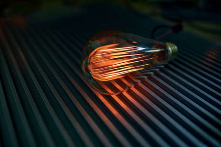 A bright fiery powerful glass incandescent lamp illuminates a dark room around with a fiery orange...