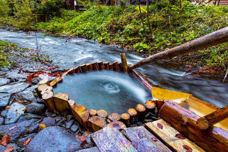 An ancient wooden old mill slowly and calmly drives the cold dark gleaming water in a frisky fast narrow river in an autumn carpathian deciduous forest, in cloudy weatherの写真素材