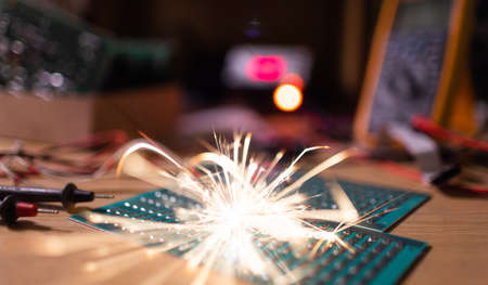 A dark green electronic printed circuit chip for TFT, with bright multi-colored wires lies on the wooden table of a talented engineer and sparkles with bright electric sparks of currentの写真素材