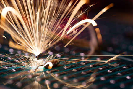 A dark green electronic printed circuit chip for TFT, with bright multi-colored wires lies on the wooden table of a talented engineer and sparkles with bright electric sparks of currentの写真素材